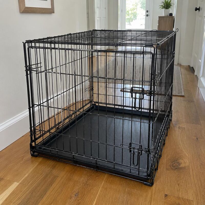 Pre-loved black folding wire dog crate in a hallway