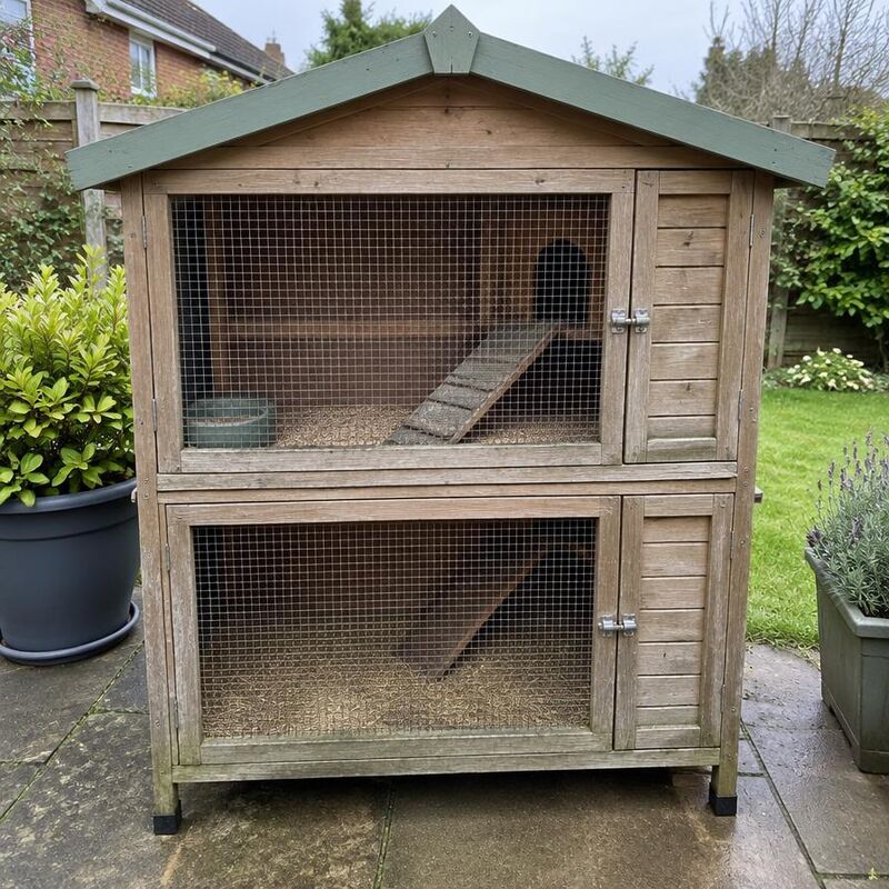 Pre-loved two-storey wooden rabbit hutch with green roof on a garden patio