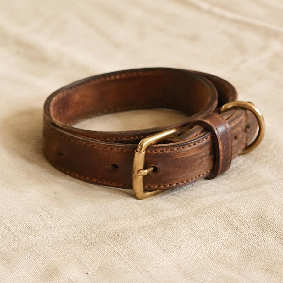 A worn brown leather dog collar with a brass buckle on linen